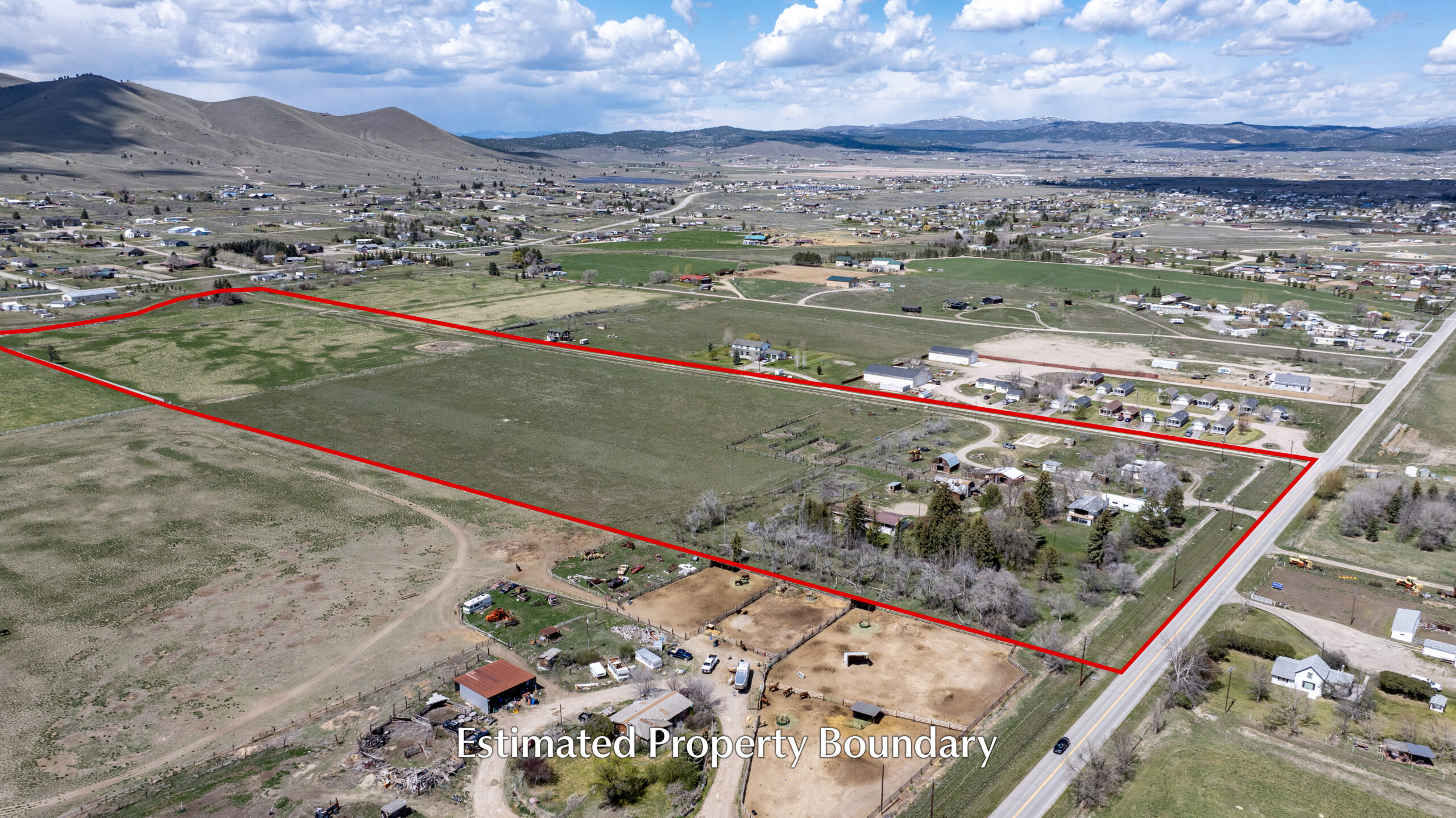 Aerial view of a large, green property outlined in red, showing fields, scattered homes, and a few outbuildings within a rural landscape under a partly cloudy sky. Text reads “Estimated Property Boundary.”.