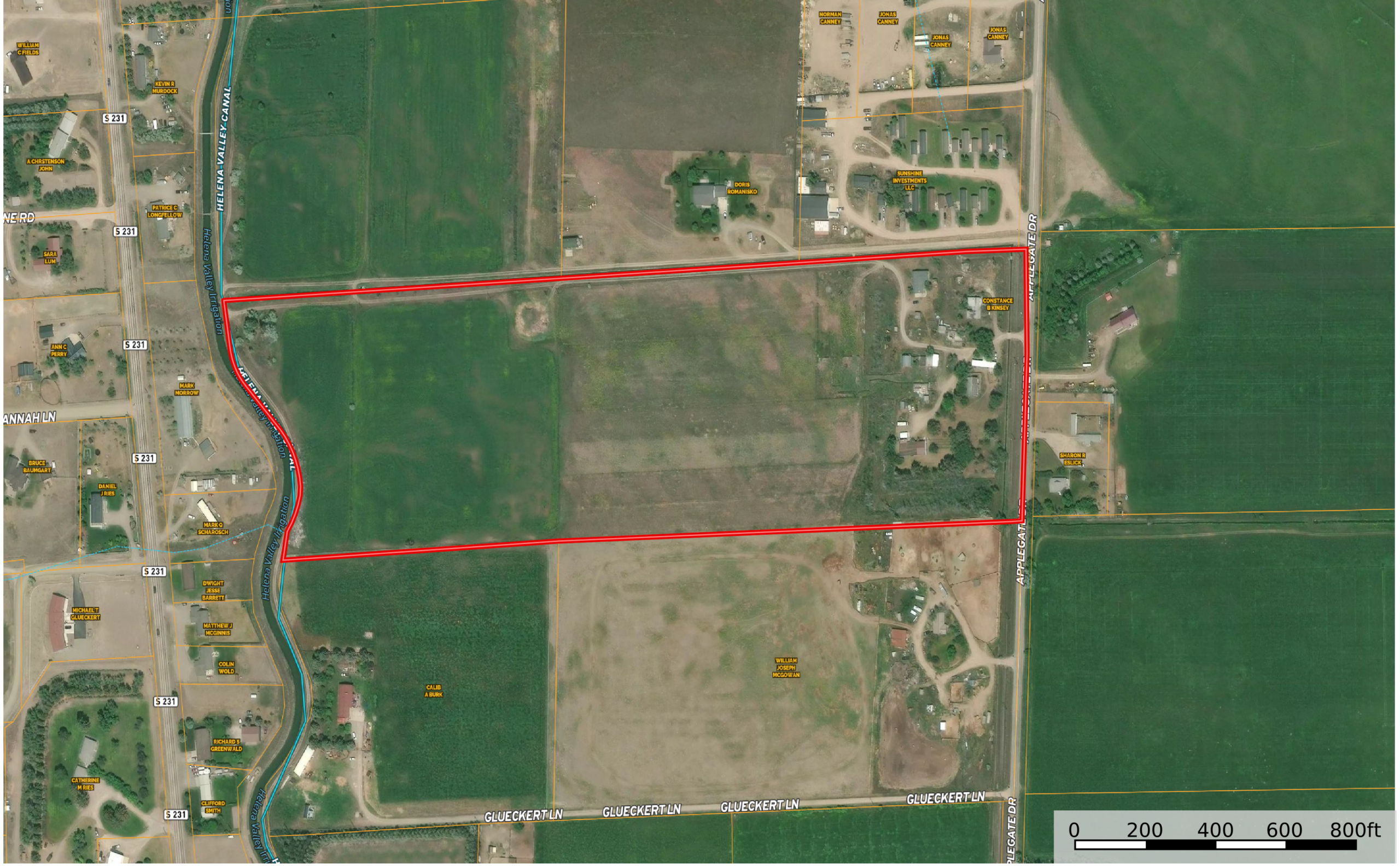 Aerial view of rural land with roads and buildings; a large, irregularly shaped area is outlined in red. Fields, houses, and vegetation surround the outlined property. A scale bar is at the bottom right.