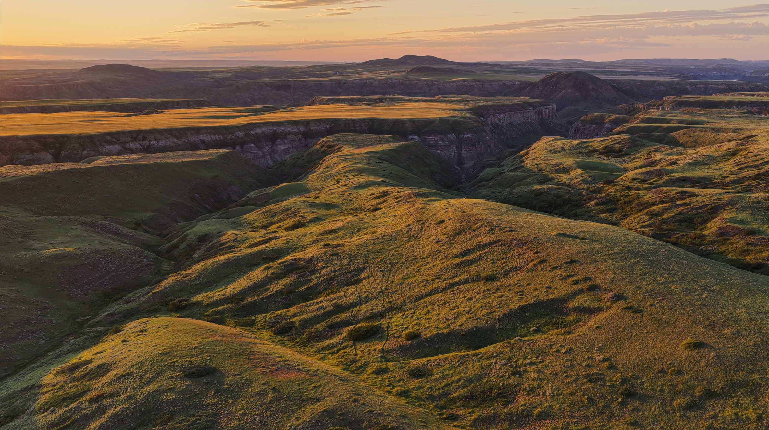 Rolling green hills and deep valleys stretch into the distance under a golden sunset sky, casting long shadows across the rugged landscape.